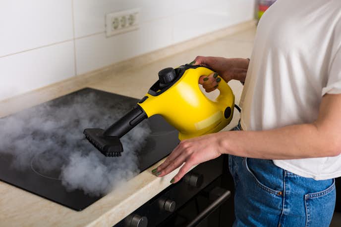 キッチンの油汚れを高温スチームクリーナーで掃除する人